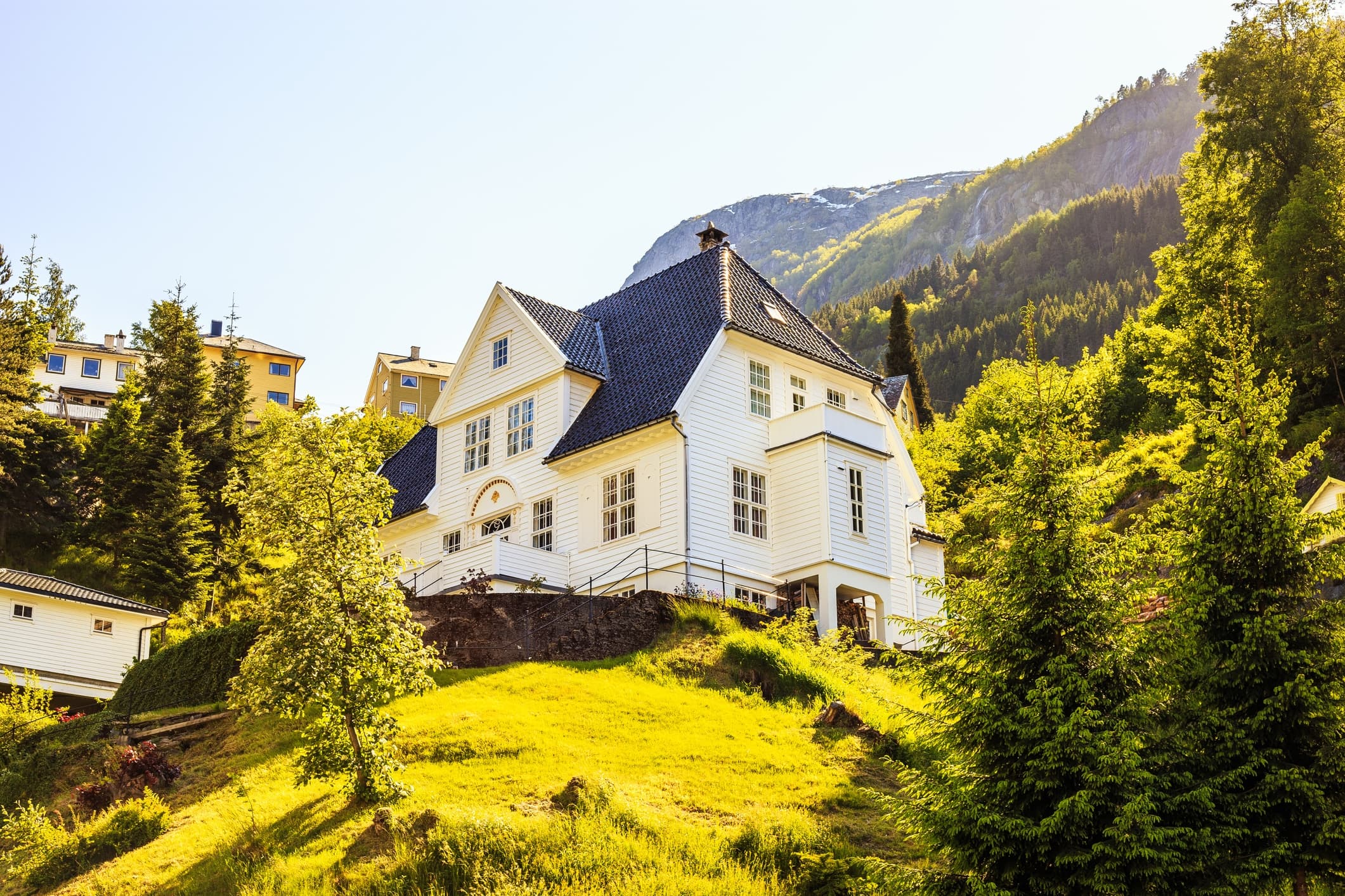 Stort hvitt trehus i Odda med mørkt tak i frodig norsk fjordlandskap, et typisk eksempel på en primærbolig