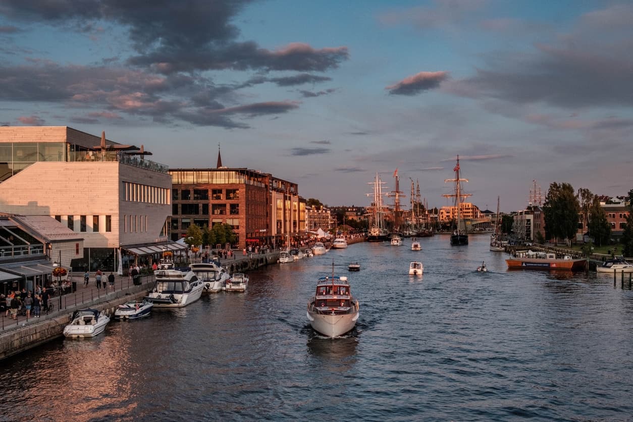 Elvebredden i Fredrikstad med båter, brygge og bebyggelse i kveldslys, illustrasjon til guide om hva en eiendomsmegler koster.