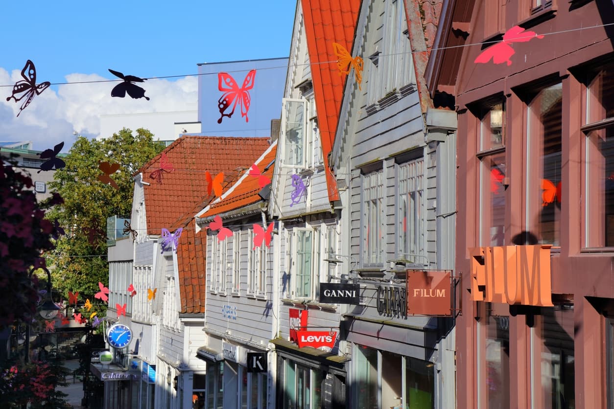 Handlegate i Stavanger sentrum med hvite trehus, røde teglstak og fargerike sommerfugler over gata, brukt i artikkel om beste eiendomsmegler på Storhaug.